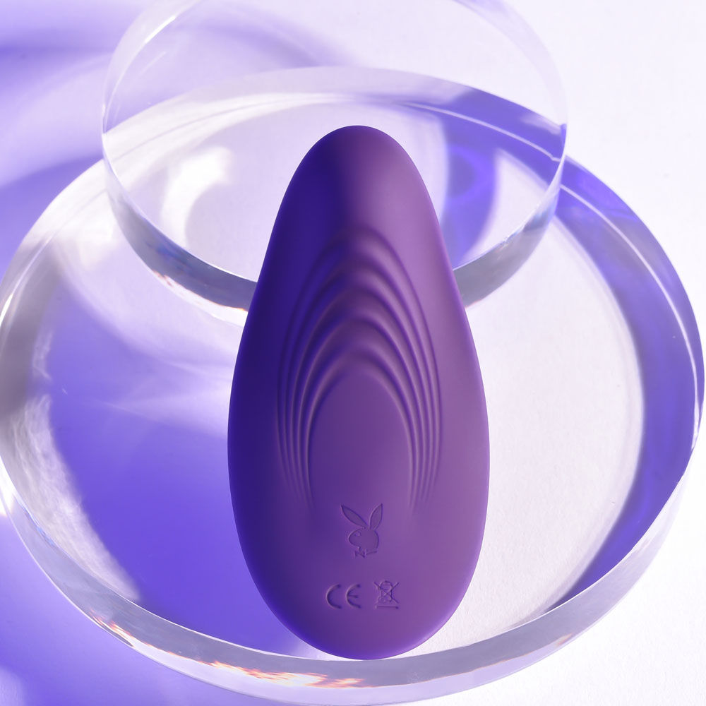 Top back view of the purple Playboy Pleasure 'Our Little Secret' vibrating panties displayed on a plexiglass bowl, set against a purple background | Flirty Bay adult store and lingerie store